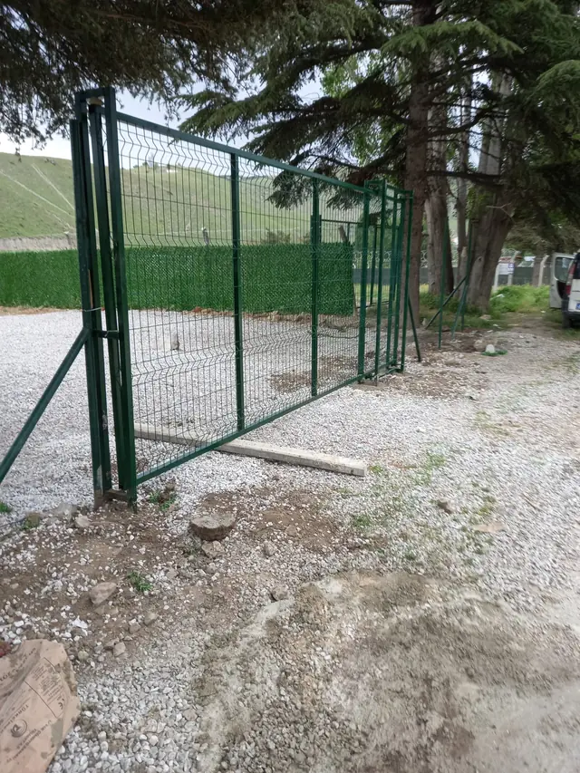 Çakıllı bahçe girişinde çift kanatlı yeşil panel bahçe kapısı