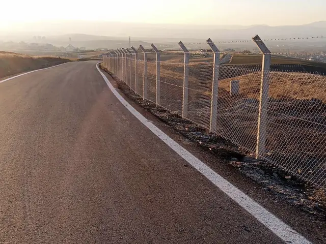 Yol kenarı boyunca beton direkli galvaniz tel örgü, direk başlarında dikenli tel kolları